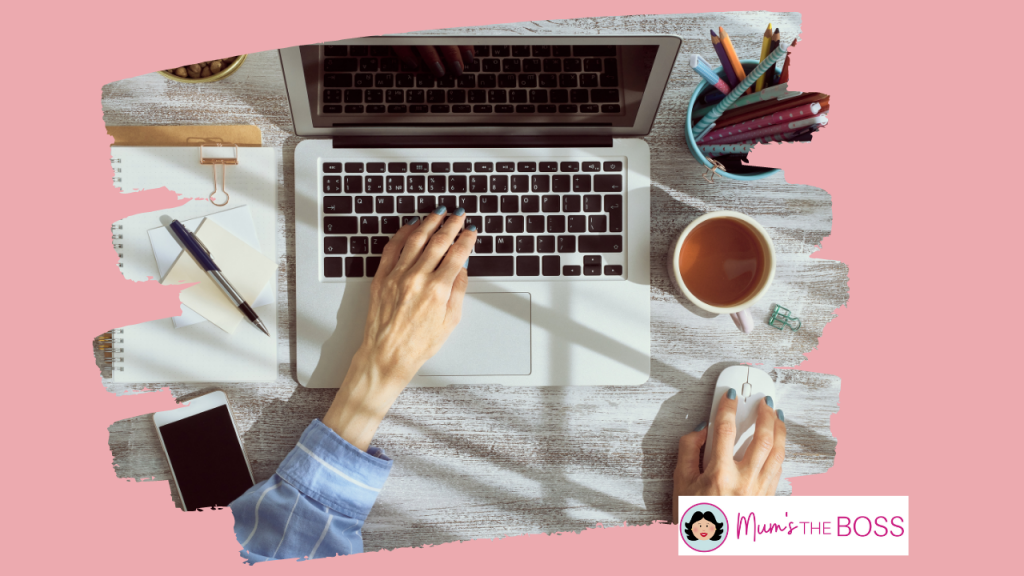 This photo is typical to illustrate the Faceless digital marketing method. You can see the nands of a woman who is sitting at a desk with a pen a phone, a laptop and some coffee  - she is using a mouse and typing on the laptop